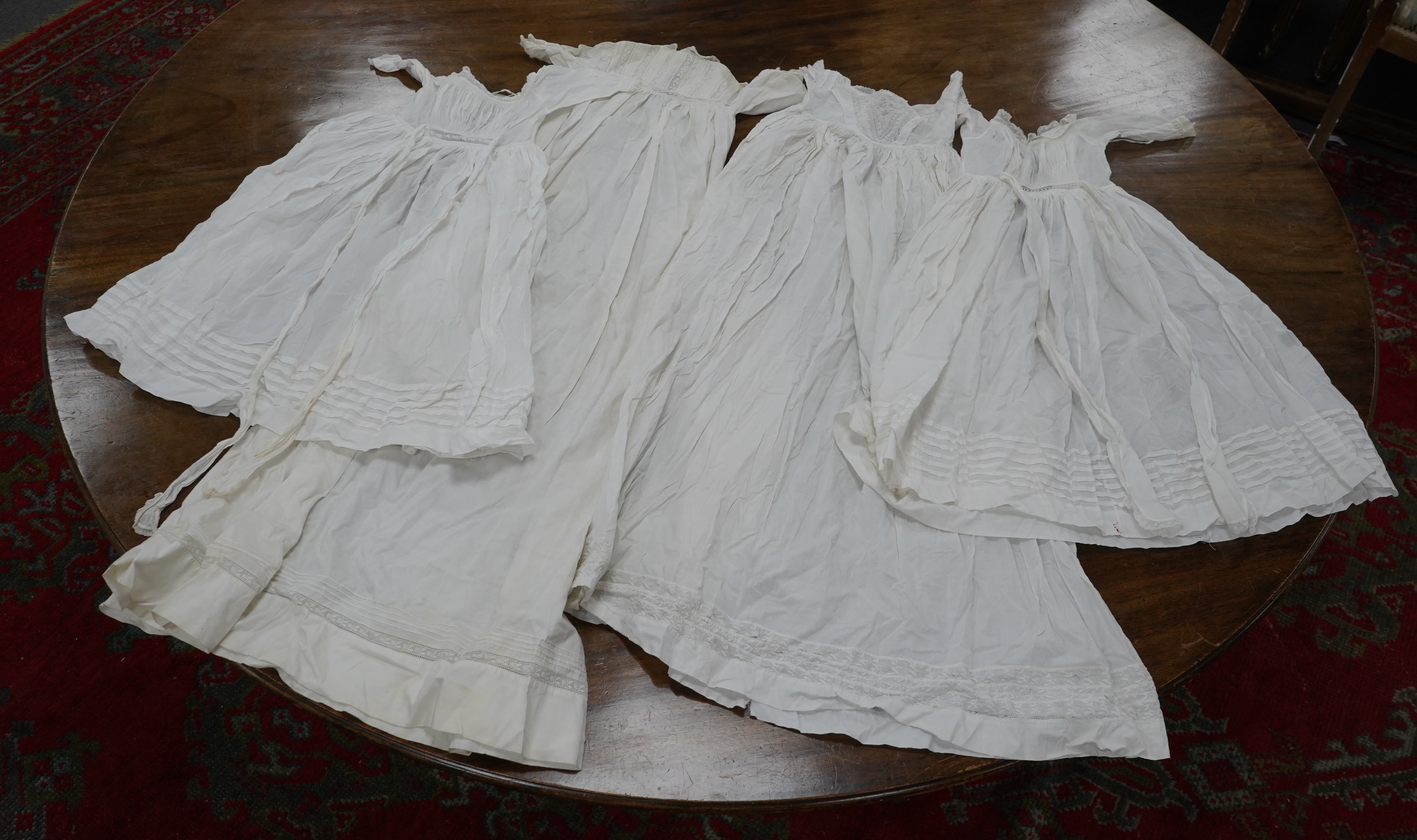 Two late 19th early 20th century long baby night gowns and two shorter baby gowns, together with a pink satin ladies full length slip and a similar cream silk stockinette slip, the bodices worked on baby dresses are embr